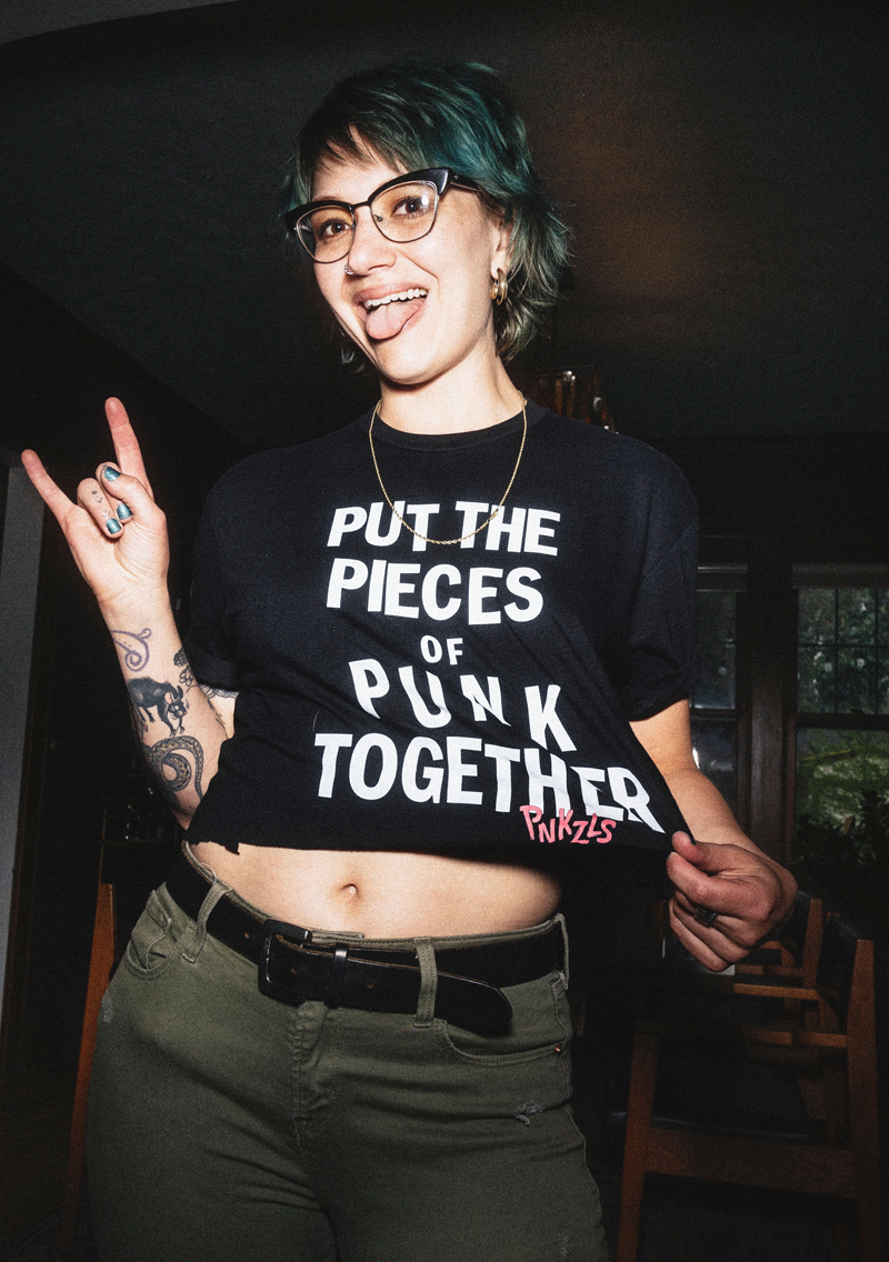 woman wearing punkzles t-shirt, making the &quot;sign of the horns&quot; hand gesture