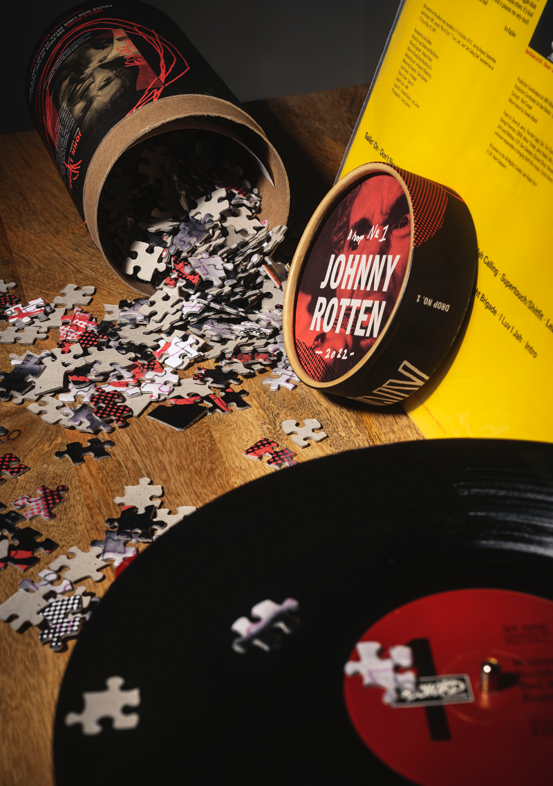 still life scene with punkzles packaging open on its side. Puzzle pieces spilling out of the open package